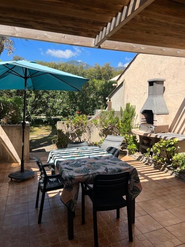 An outdoor patio with a table and chairs, a green umbrella, and a stone chimney.