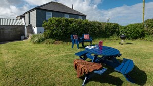 Una casa con facciata blu, un giardino anteriore con tavolo e sedie da picnic e un barbecue.