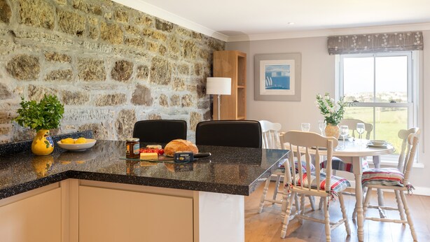 Una cucina con parete in pietra, zona pranzo con sedie e tavolo, e finestra con vista.