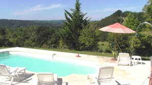A swimming pool with lounge chairs and a red-striped umbrella. - In the center of Périgord  Noir (SARLAT 20 Km)- LE COUX et BIGAROQUE.  Périgourdine house with  swimming pool, beautiful panorama on valley, on property of 6 ha. (Coux Et Bigaroque-Mouzens)