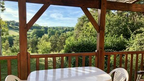 A wooden deck with a white table and chairs, overlooking a lush green landscape. - In the center of Périgord  Noir (SARLAT 20 Km)- LE COUX et BIGAROQUE.  Périgourdine house with  swimming pool, beautiful panorama on valley, on property of 6 ha. (Coux Et Bigaroque-Mouzens)