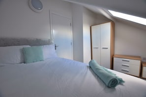 Een slaapkamer met een bed, nachtkastje, garderobe en dakraam.