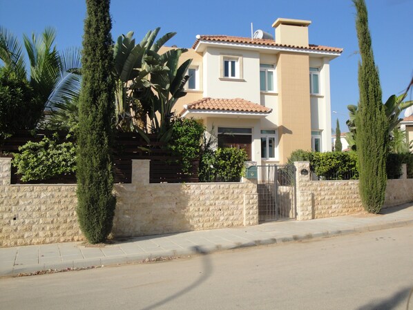 A two-story residential building with a stone wall, a tiled roof, and a gated entrance.