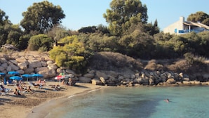 Ein Strand mit klarem Wasser, badenden Personen und Sonnenschirmen im Sand.