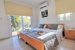 A bedroom with a bed, two bedside tables, a nightstand, a window, and an air conditioning unit.