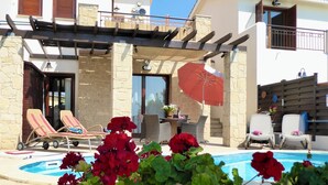 A poolside area with lounge chairs, a red umbrella, and a stone wall. - 'Villa Xenia' HG 25  Play golf, tennis or relax in the spa (Aphrodite Hills)