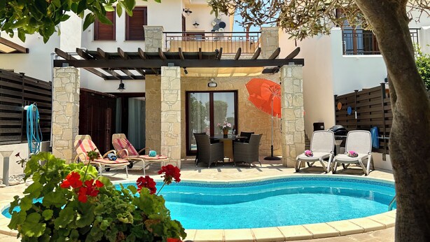 A pool area with lounge chairs, a pergola, and a stone wall. - 'Villa Xenia' HG 25  Play golf, tennis or relax in the spa (Aphrodite Hills)