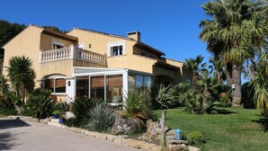 A two-story house with a balcony, a conservatory, and a well-maintained garden with palm trees and other plants. - Beautiful villa with garden, swimming pool and jacuzzi close to all amenities (La Farlède)