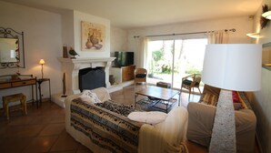 A living room with a sofa, a coffee table, a fireplace, a television, and a large window with curtains. - Beautiful villa with garden, swimming pool and jacuzzi close to all amenities (La Farlède)