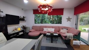 A modern living room with a pink sofa, a flat-screen TV, a coffee table, and a large window with a view of greenery. - Villa with pool and fun Ría de Vigo (Muiño, O (Cobres))