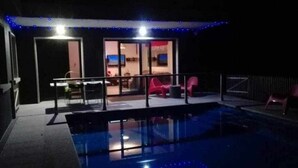 A swimming pool area with a glass barrier, a red chair, and a room with a TV visible through the glass doors. - Villa with pool and fun Ría de Vigo (Muiño, O (Cobres))