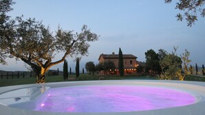 A pool with a purple-lit edge, surrounded by trees and a house in the background. - Casa di Campagna Colline Senesi San Giovanni in Poggio - app. Twilight Siena (Monteroni d'Arbia)