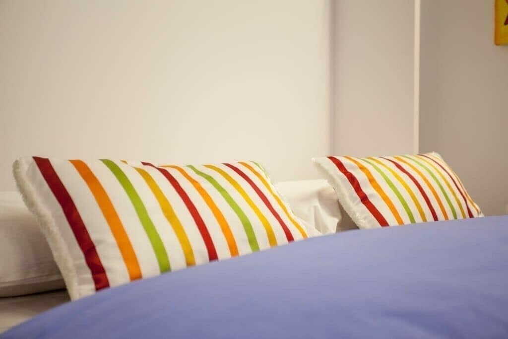 A bed with a blue cover and two pillows with multicolored stripes.