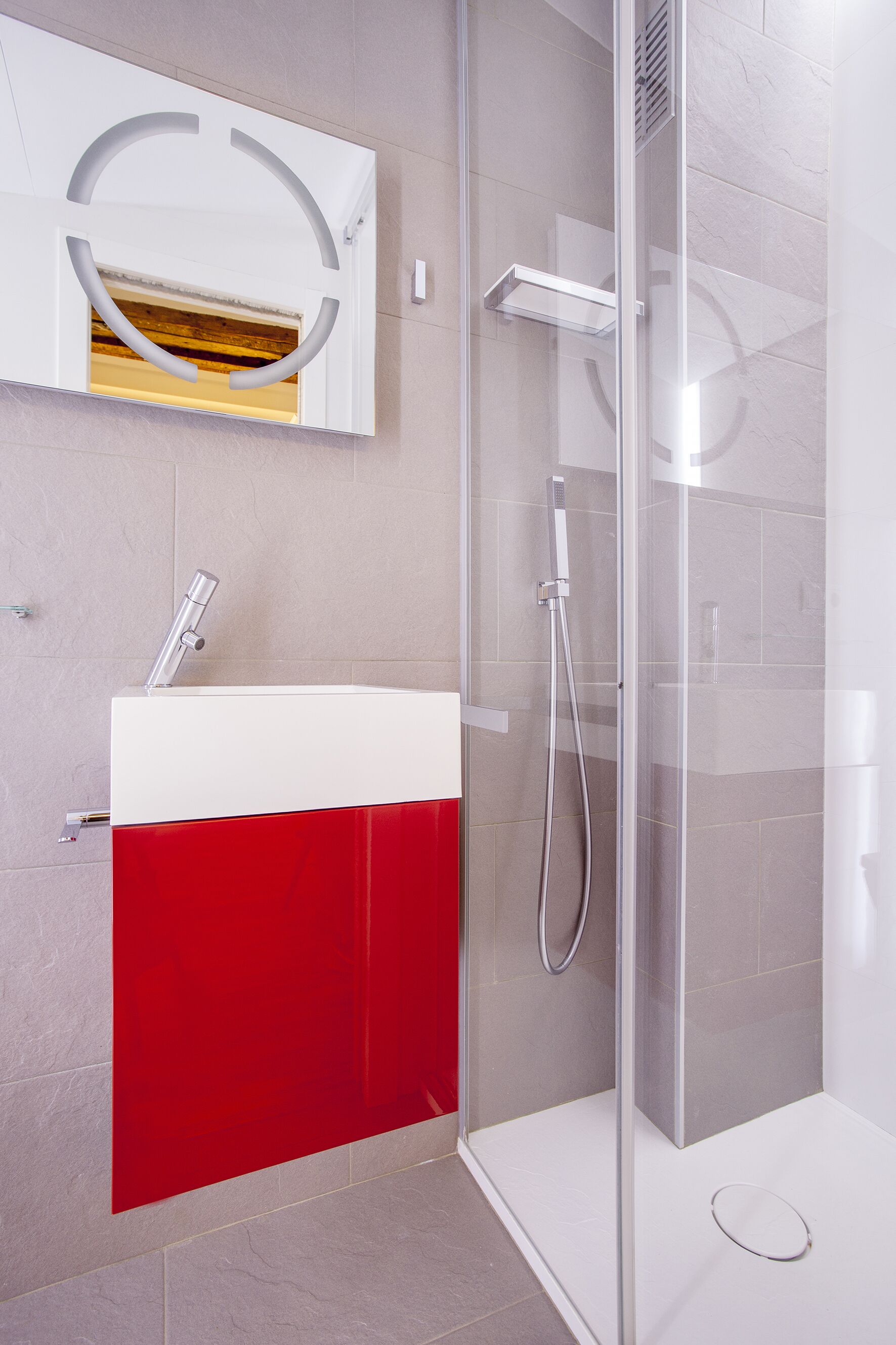 Un baño moderno con ducha envuelta en vidrio, un lavamanos blanco y armarios rojos.