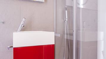 Un baño moderno con ducha envuelta en vidrio, un lavamanos blanco y armarios rojos.