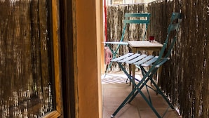 A narrow outdoor corridor with a wooden door, a table with chairs, and a view of buildings in the background. - CHARMING STUDIO AT THE CATHEDRAL. (STRICTLY TWO PEOPLE) (València)