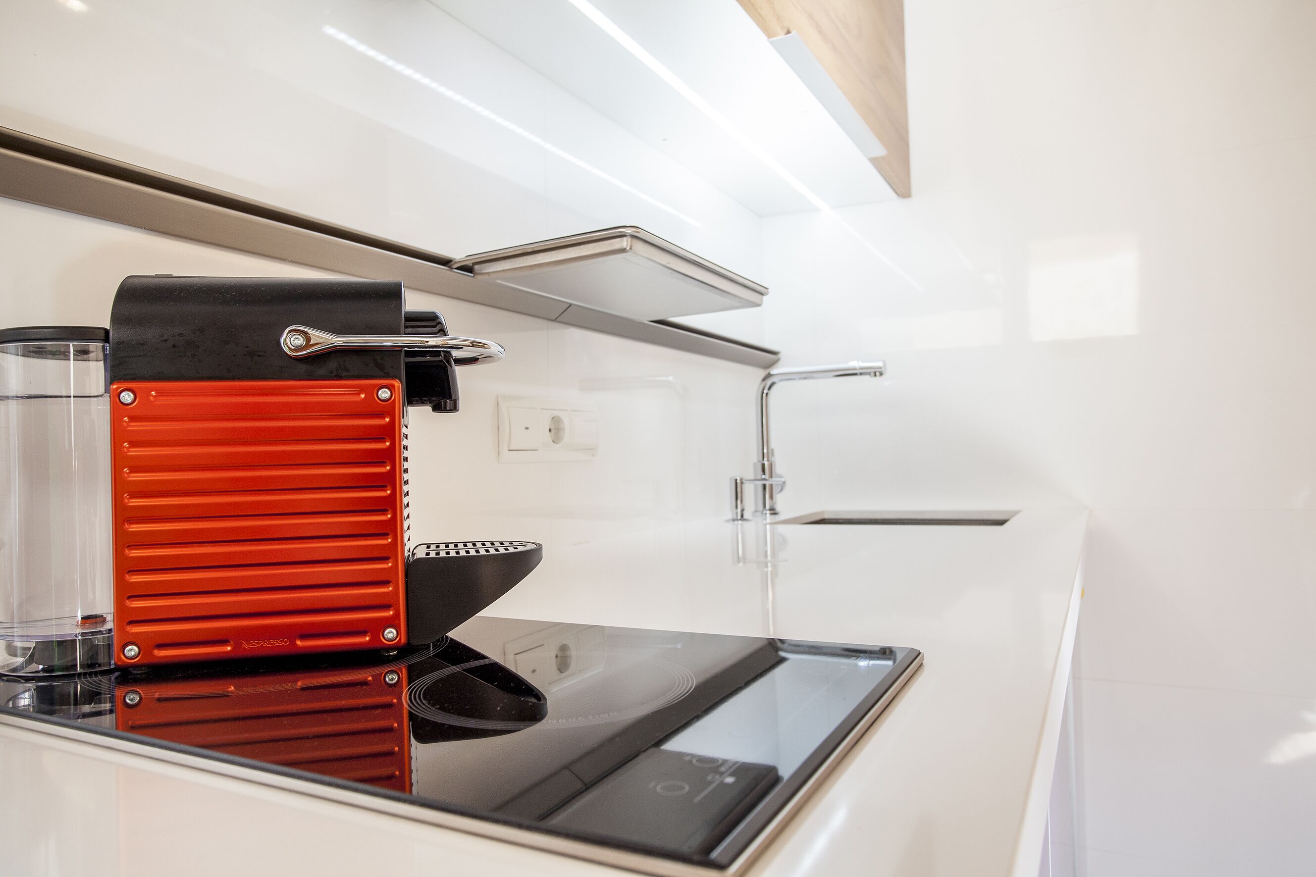 Una cocina compacta con una cafetera espresso moderna, un lavamanos y un horno empotrado.
