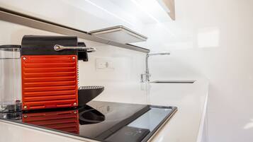 Una cocina compacta con una cafetera espresso moderna, un lavamanos y un horno empotrado.