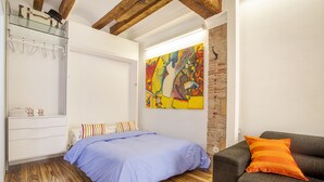 A bedroom with a bed, a wardrobe, a colorful abstract painting, a grey sofa, and a wooden floor. - CHARMING STUDIO AT THE CATHEDRAL. (STRICTLY TWO PEOPLE) (València)
