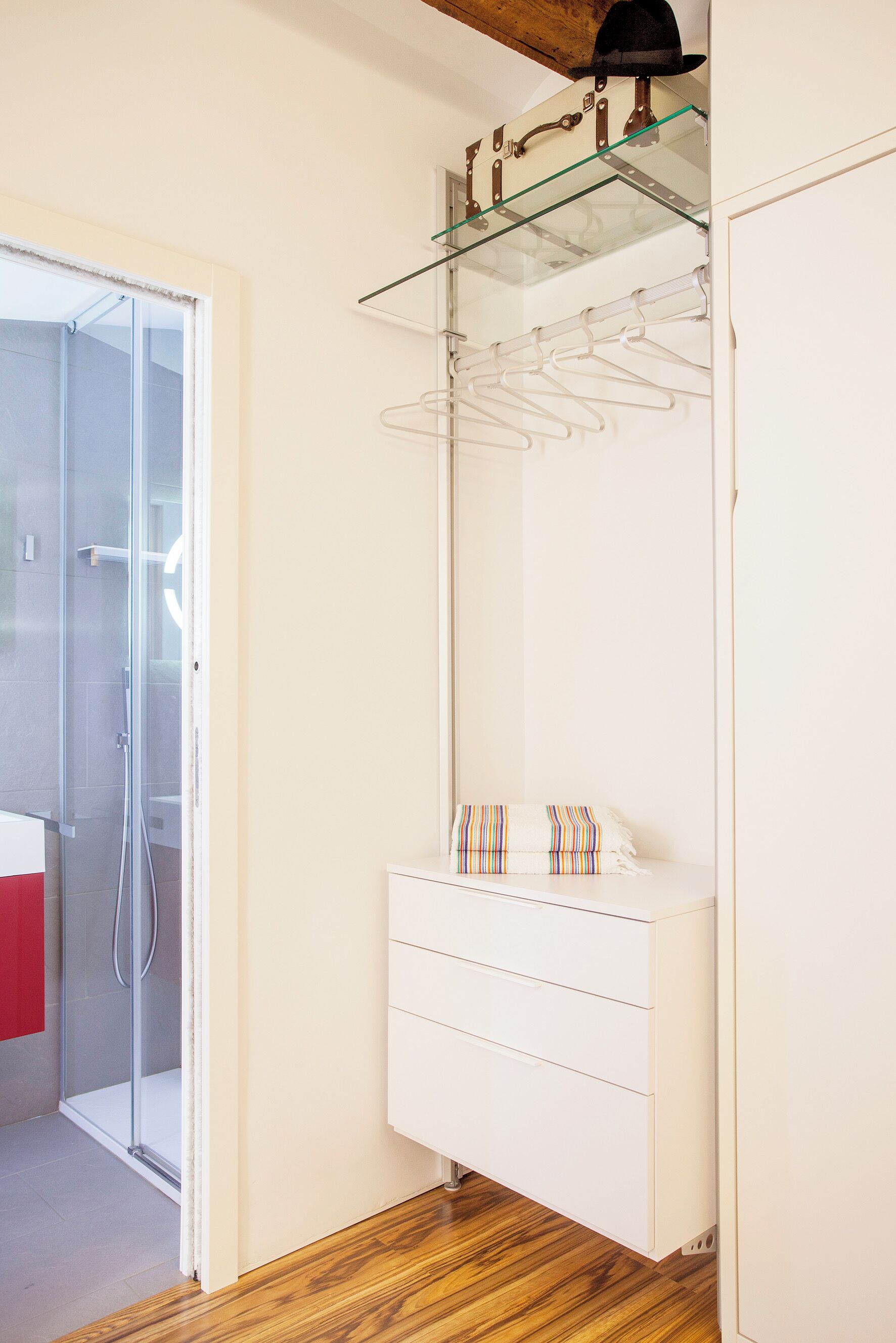 Un baño moderno con cabina de ducha de vidrio, tocador blanco con espejo y suelo de madera.