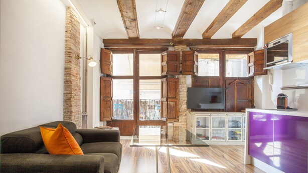 A modern living room with a sofa, a glass coffee table, and a kitchen area with wooden cabinets and a refrigerator. - CHARMING STUDIO AT THE CATHEDRAL. (STRICTLY TWO PEOPLE) (València)