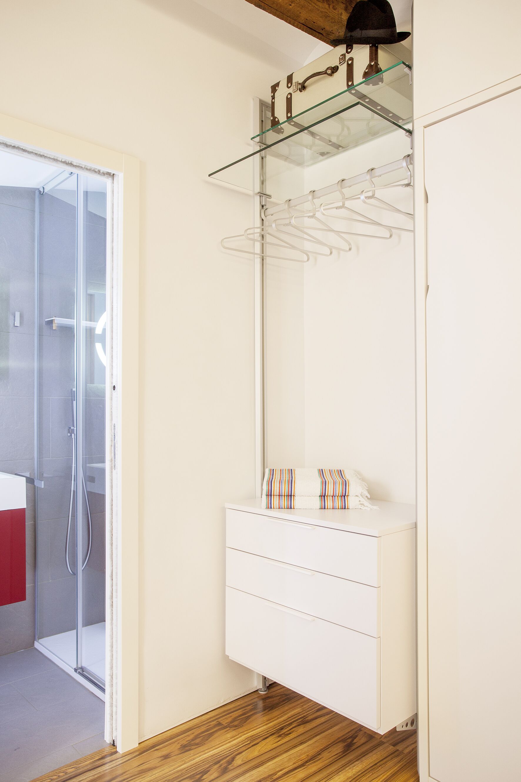 Un baño moderno con cabina de ducha de vidrio, un tocador blanco con espejo y piso de madera.