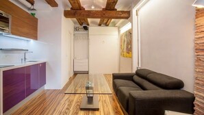 A modern kitchen with wooden beams, a glass-top dining table, and a dark sofa in a living area. - CHARMING STUDIO AT THE CATHEDRAL. (STRICTLY TWO PEOPLE) (València)