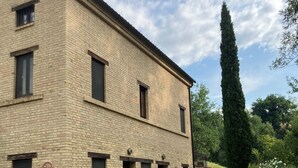 Un bâtiment en briques de deux étages, doté de nombreuses fenêtres et d’un petit jardin agrémenté de plantes en pot.