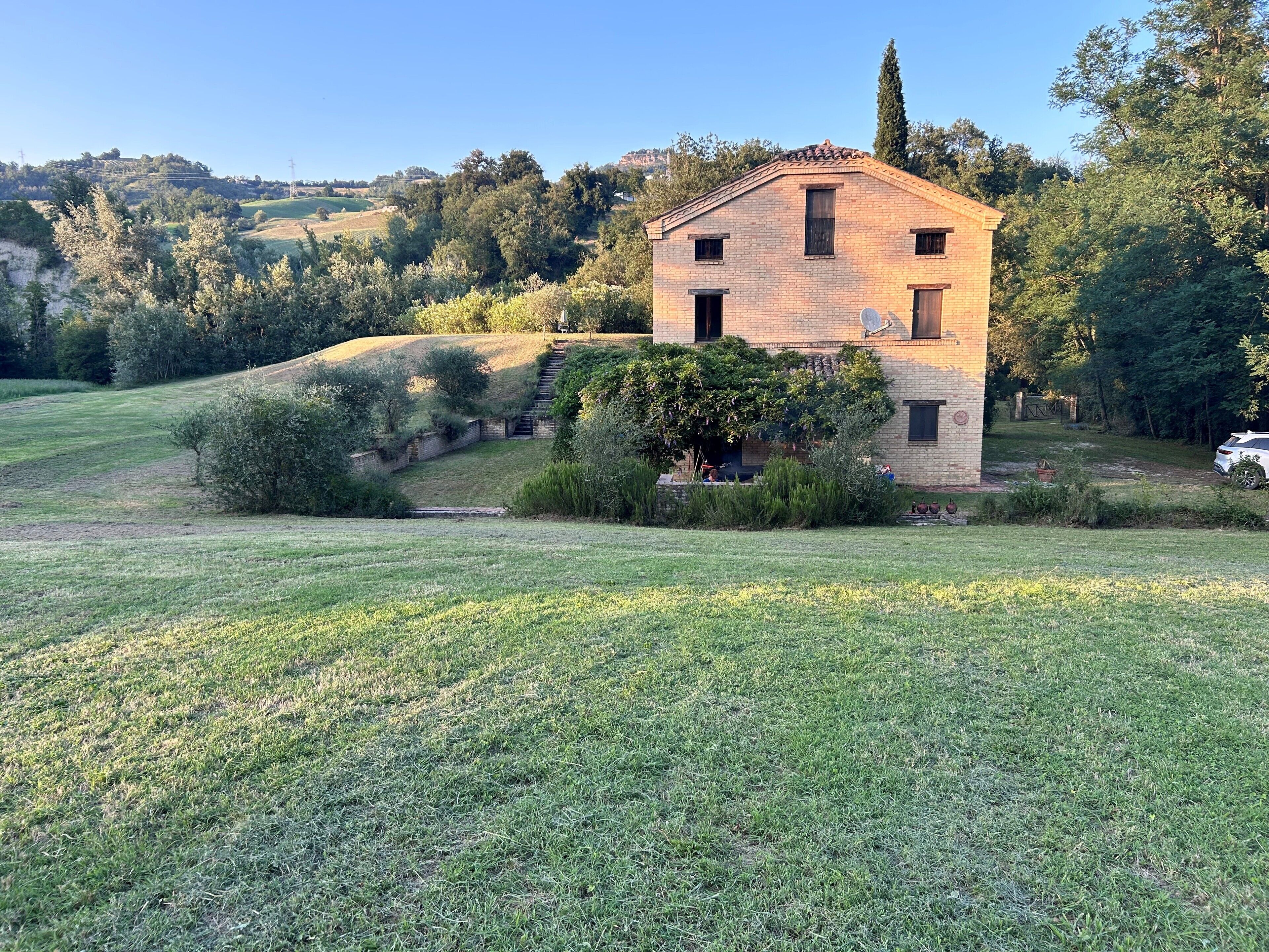 Una casa a un piano in mattoni con tetto spiovente, immersa in un prato erboso e alberi.