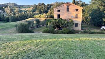 Una casa a un piano in mattoni con tetto spiovente, immersa in un prato erboso e alberi.
