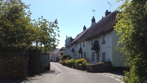 Une rue étroite bordée de maisons blanches traditionnelles aux toits de chaume, un ciel dégagé et un regard d’égout sur la chaussée.