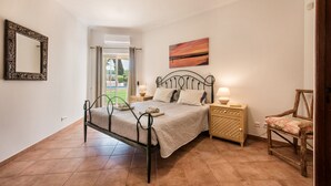 Un dormitorio con cama, mesitas de noche, una silla, un espejo y un cuadro.