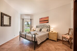 Un dormitorio con cama, mesitas de noche, una silla, un espejo y un cuadro.