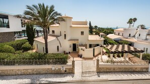 Una villa de estilo mediterráneo con piscina, palmeras y un muro de piedra.