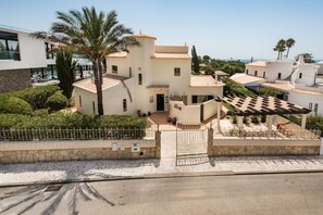 Una villa de estilo mediterráneo con piscina, palmeras y un muro de piedra.