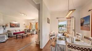 Amplia sala de estar con mesa de desayuno, un sofá y vistas al exterior.