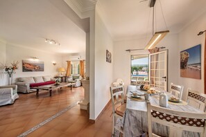 Amplia sala de estar con mesa de desayuno, un sofá y vistas al exterior.