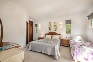 Une chambre à coucher avec un lit double, une table de chevet avec une lampe, une armoire en bois et une fenêtre donnant sur un paysage verdoyant.