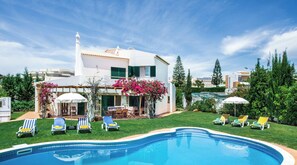 A two-story house with a swimming pool, outdoor seating, and greenery.