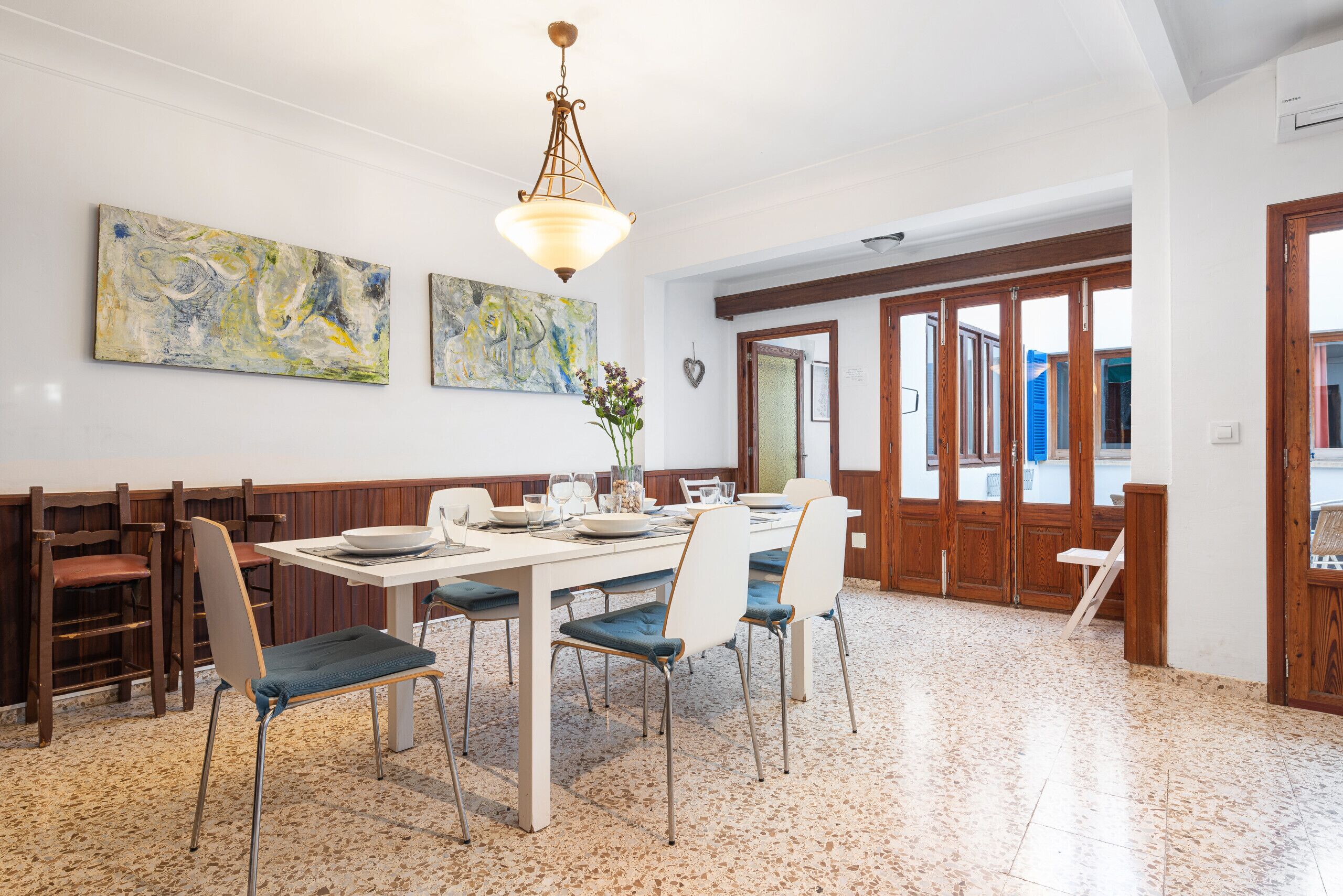 A dining area with a white table, blue cushioned chairs, and a hanging light fixture.