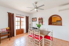 A dining area with a wooden table and chairs, a ceiling fan, and a view of the kitchen through an archway.