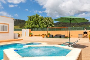 A rooftop pool area with a hot tub, lounge chairs, and an umbrella.