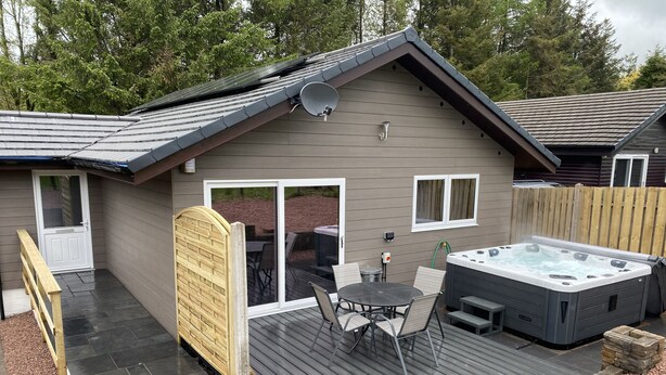 Une maison dotée d’une terrasse, d’un jacuzzi et d’un espace extérieur avec des chaises et une table.