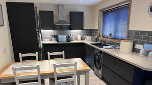 Une cuisine moderne avec un coin repas, comprenant un lave-linge encastré, une fenêtre avec stores et un crédence carrelée.