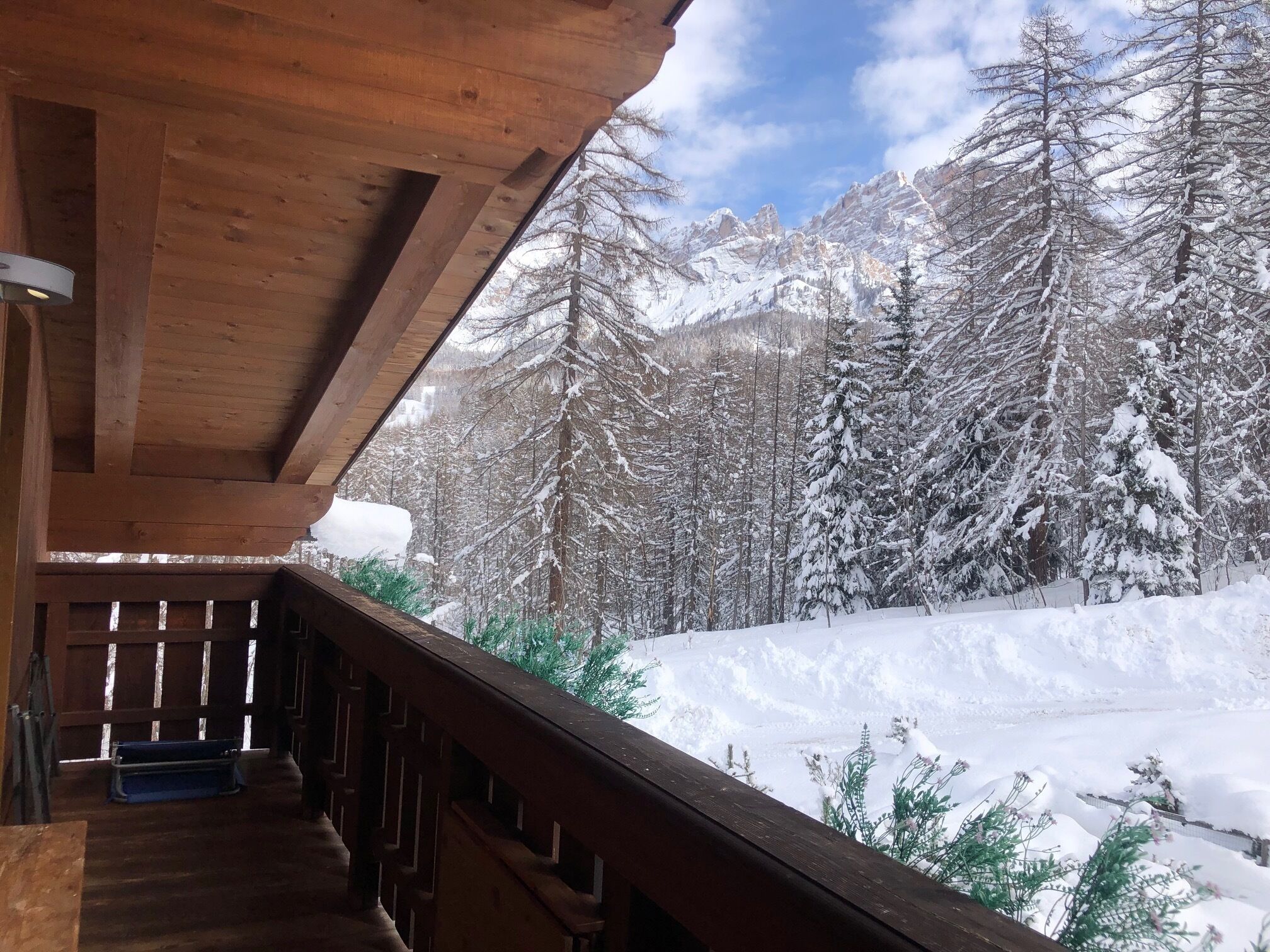 Une cabane en bois avec un escalier menant à un balcon d’où l’on peut admirer une forêt et des montagnes recouvertes de neige.