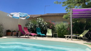 Ein Pool mit Liegestühlen und Sonnenschirmen, umgeben von Grünpflanzen und einem Gebäude mit Ziegeldach.