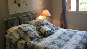 Ein Schlafzimmer mit einem Bett, einem Wandbild, einem Fenster mit Vorhängen und einer Nachttischlampe.