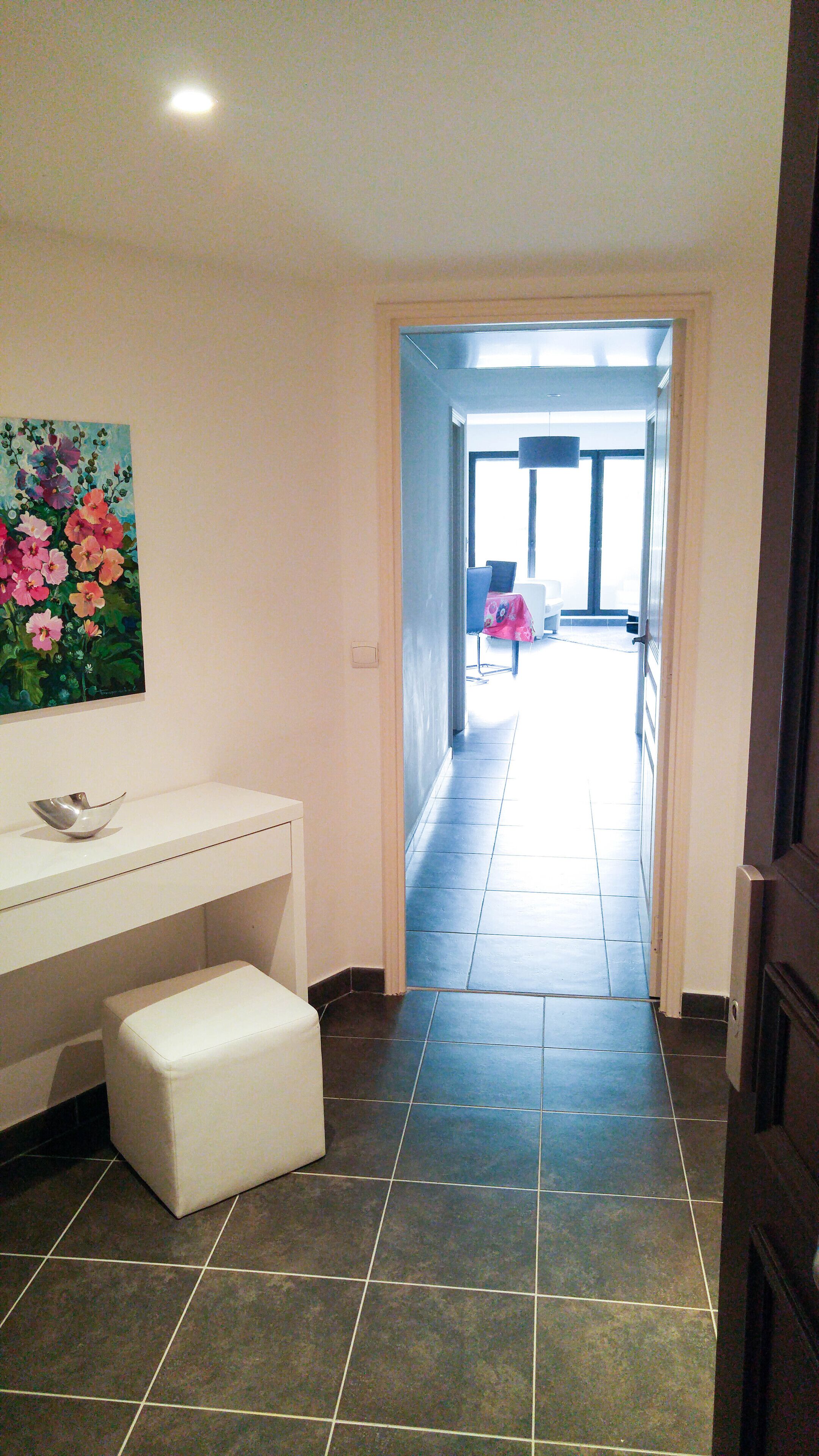 A hallway with a white bench, a painting of flowers on the wall, and a view into a dining area.