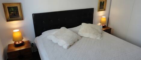Un lit bien fait, recouvert d’une couette blanche matelassée et agrémenté de deux coussins décoratifs, avec deux tables de chevet de chaque côté, sur lesquelles sont posées des lampes.