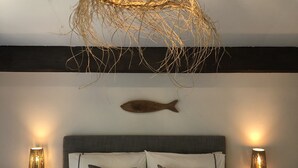 Un dormitorio con una cama grande, dos mesitas de noche con lámparas, un pez decorativo en la pared y una lámpara colgante tejida sobre la cama.